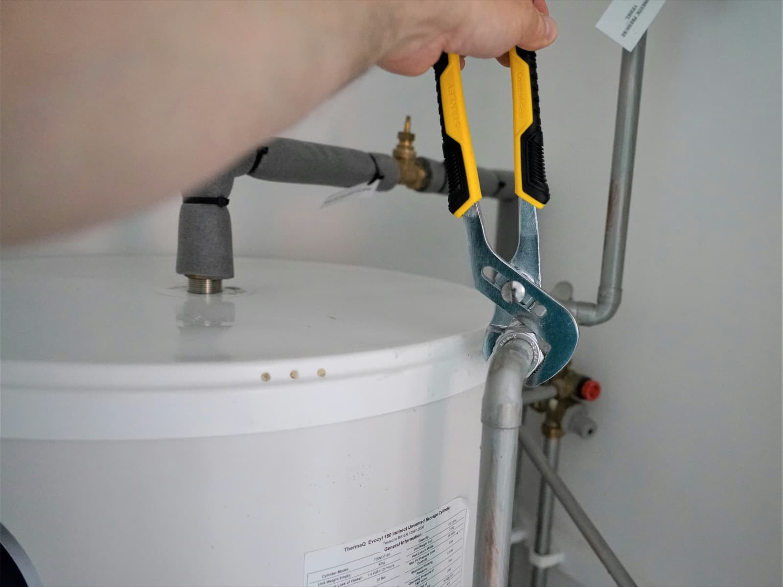 Plumber using channel-lock pliers on the supply line fitting of a tank water heater