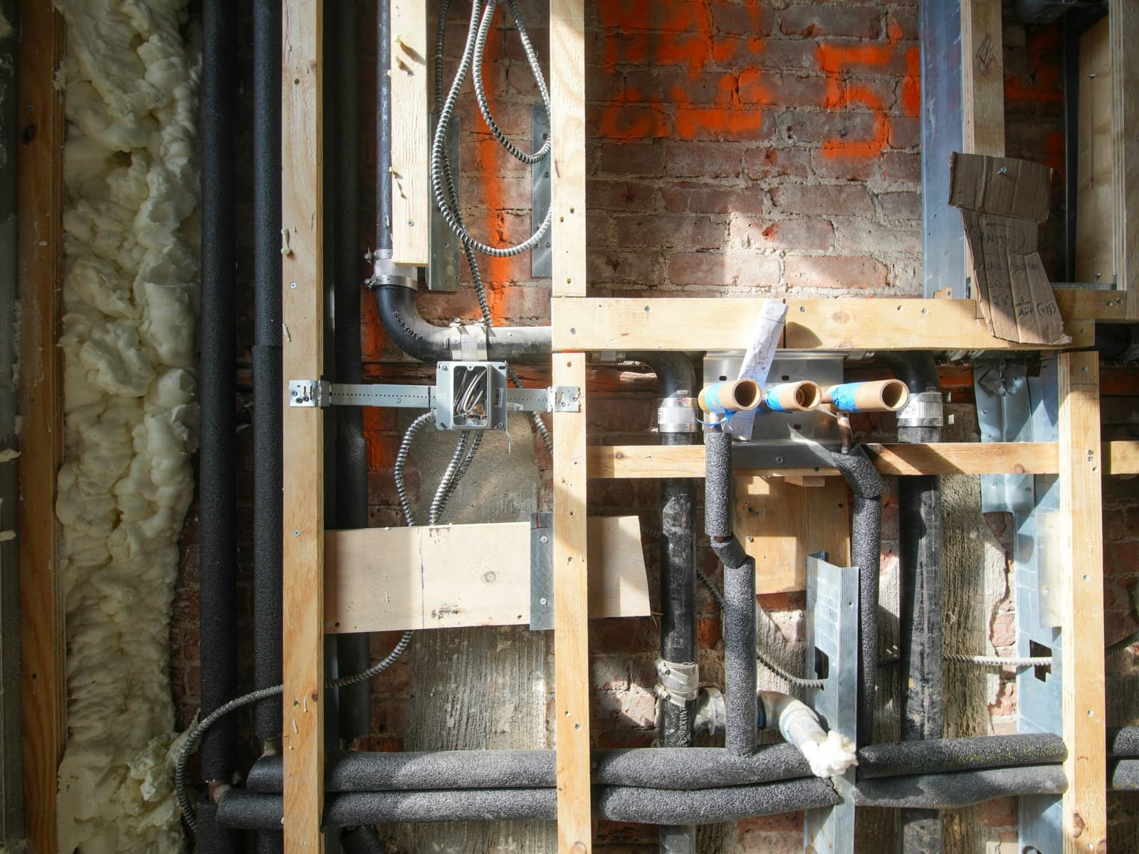 Open wall framing with new insulated water supply lines and drain pipes during a repipe